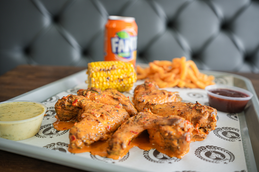 Peri peri chicken wings served with corn on the cob, seasoned fries, dipping sauces, and an orange Fanta on a tray at Poco Loco Peri Peri Takeaway Wishaw