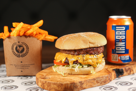 Cheeseburger with fresh toppings served with seasoned fries and a can of IRN-BRU on a wooden board at Poco Loco Peri Peri Takeaway Wishaw